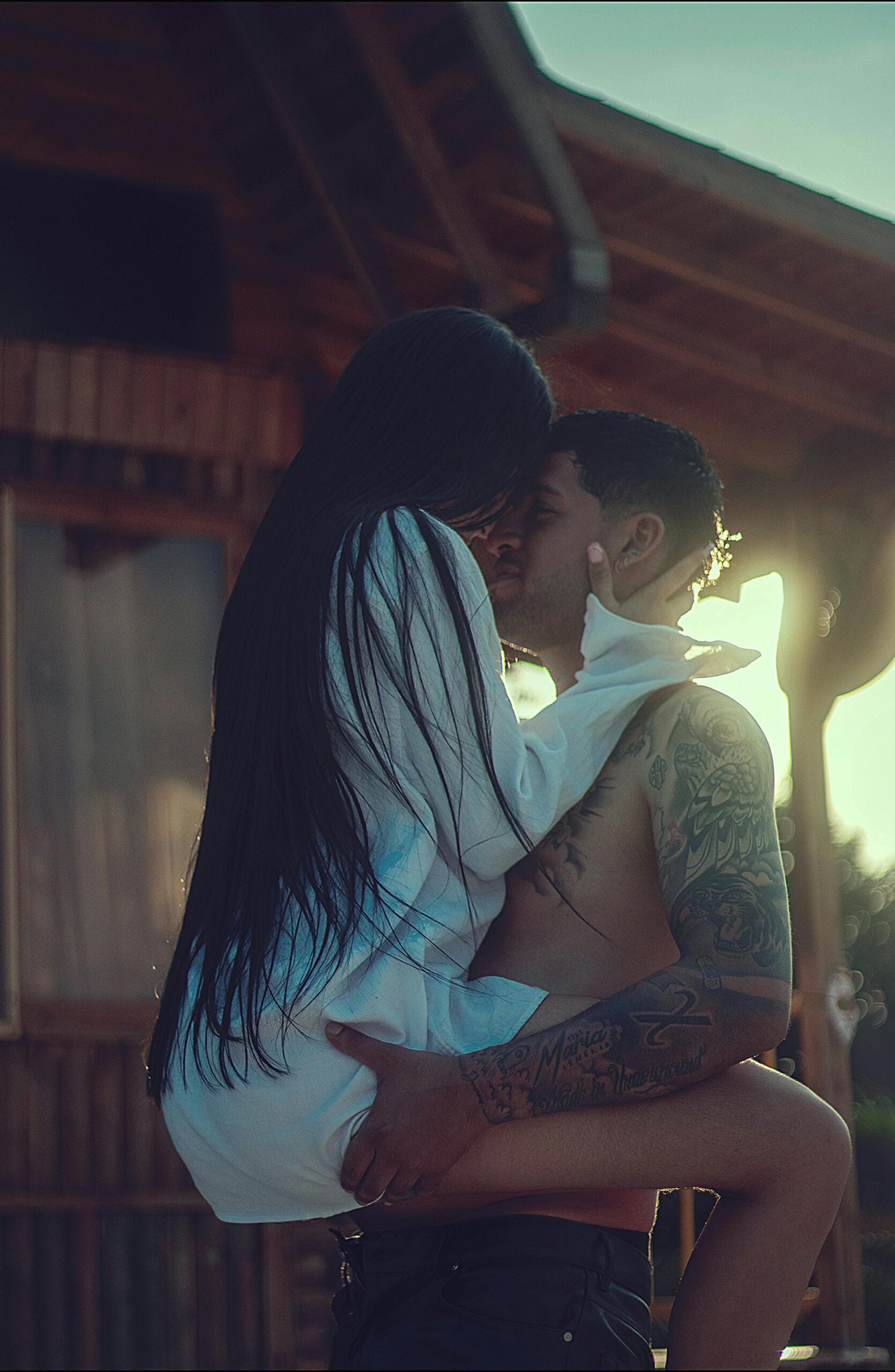 Tender moment between a young couple embracing outside a rustic cabin during sunset.